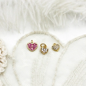 Detailed view of 18K gold heart charms with magenta and white cubic zirconia on white lace