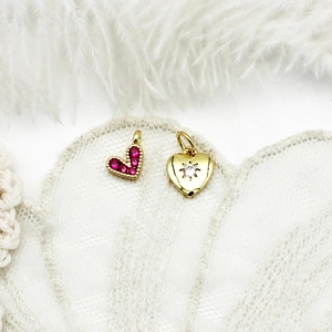 Macro detail of micro-pave red heart charm and 18K gold starburst pendant with stones