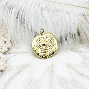 Detailed view of an 18K gold plated vintage bee coin pendant with JW engraving on lace