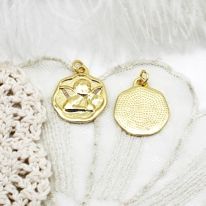 Macro detail of 18K gold plated angel charms with relief design on lace background