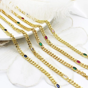 Detailed view of golden Cuban link bracelets with multi-colored oval gemstones and white feathers