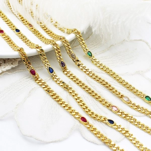 Close-up of golden Cuban link chains with colorful pear-cut zircon pendants and lace