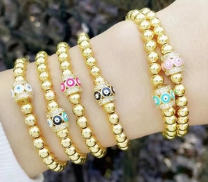 Dettaglio di bracciali a sfere dorate con ciondoli occhio greco in smalto colorato