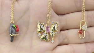 Detailed view of 18K gold plated bow and heart pendants held in palm for size scale