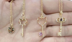 Detail of 18K gold plated heart and key pendants with colorful zircon inlay on a hand