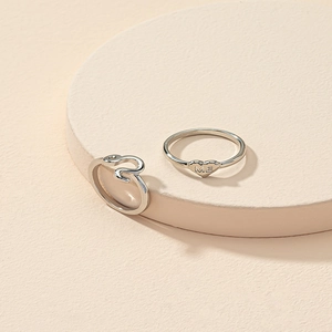 Silver heart ring set with ME engraving and abstract curved band on minimalist display