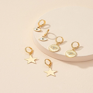 Tre paia di orecchini d'oro minimalisti con pendenti a stella e occhio su piedistallo
