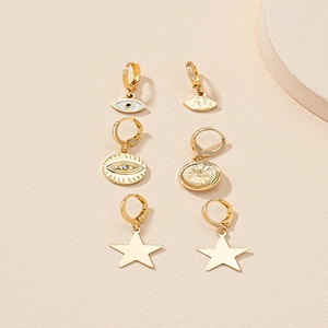 Set di tre paia di orecchini a cerchio dorati con stella e occhio su sfondo beige