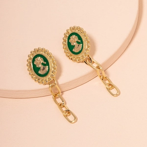 Close-up of vintage gold earrings with green enamel portrait and chunky chain details