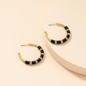 Close-up of C-shaped gold hoop earrings featuring black and gold bohemian disc beads