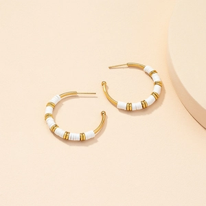 Detail of C-shaped gold hoops with white Heishi beads and cylindrical spacers on a beige background