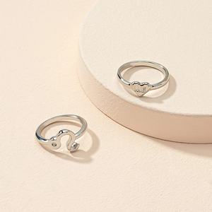 Macro shot of silver heart ring with ME engraving and Leo zodiac sign ring on beige stand