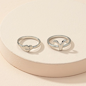 Detailed shot of silver Aries zodiac and heart motif rings on a beige platform