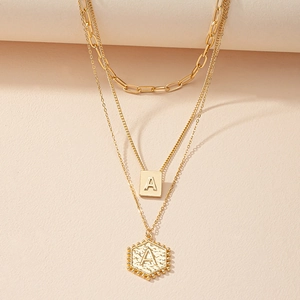 Detail van gelaagde gouden ketting met rechthoekige en zeshoekige hangers met de letter A