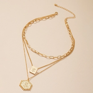 Detail van gelaagde gouden ketting met drie kettingen en gegraveerde letter S-hangers
