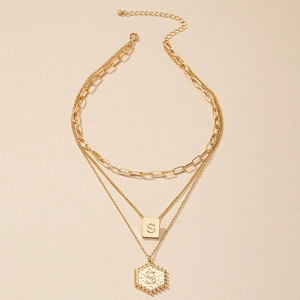 Detailopname van de drielaagse gouden ketting met gegraveerde hangers en de letter S