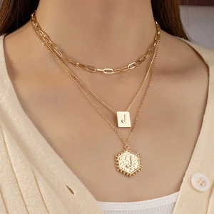 Detail van de drielaagse gouden ketting met letter J hangers en getextureerde plaatjes