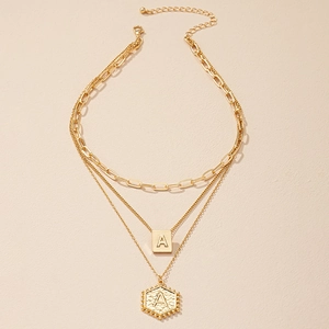Detail van drielaagse gouden ketting met vierkante en zeshoekige letter A hangers