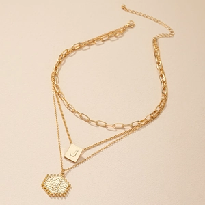 Detail van drielaagse gouden ketting met J-letter vierkante en zeshoekige hangers