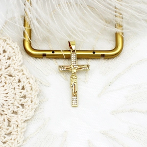 Macro del ciondolo a croce dorata con zirconi micro-pave su pizzo bianco e piume