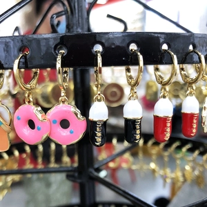 Detail van roze donut en Happy-pil hangers aan gouden oorringen voor dames