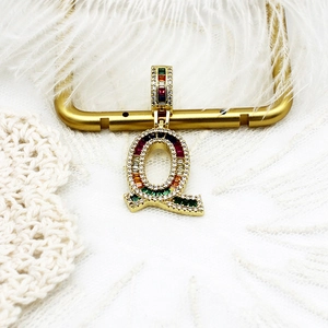 Vue macro du pendentif lettre Q plaqué or 18k avec zircons arc-en-ciel et plumes blanches