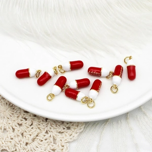 Macro shot of red and white enamel capsule charms with golden jump rings for DIY jewelry