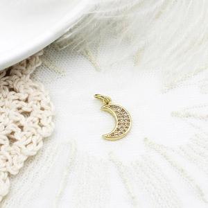 Detailed view of a gold crescent moon pendant with micro-pave crystals on white lace