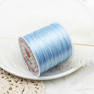 Macro detail of light blue elastic beaded cord spool on a white decorative background