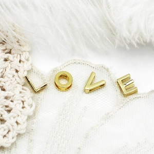 Goldene LOVE Buchstabenperlen für DIY-Schmuck auf weißem Spitzen- und Federhintergrund