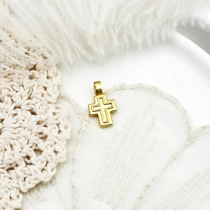 Macro shot of gold cross pendant with indented lines on soft white feather background