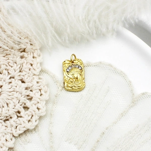 Golden Virgin Mary pendant with white stones on beige lace and feather background