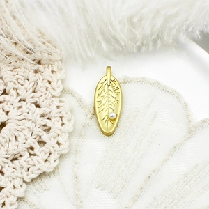 Golden leaf pendant with fine texture and white pearl detail on woven background
