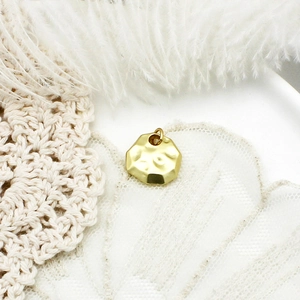 Detail of matte gold polygonal charm with hand-hammered texture on lace and feather fabric