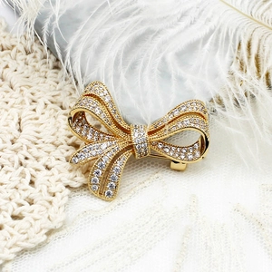 Elegant gold bow brooch with micro-pave crystals on white feather and lace background