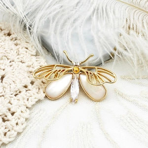 Broche papillon dorée élégante avec incrustation de nacre blanche sur fond de dentelle