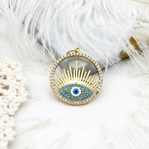 Dettaglio del ciondolo tondo occhio di Allah in oro 18k con zirconi su sfondo pizzo
