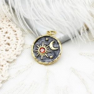 Detail of 18K gold plated sun and moon pendant with a red gemstone and enamel