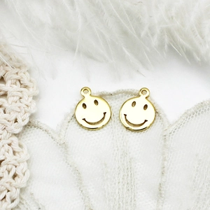 Macro detail of 18K gold plated smiling face charms on white lace and feather background