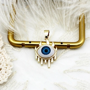 Macro shot of 18K gold evil eye charm with blue core on a white feather background