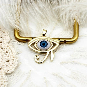 Detail of 18K gold-plated Horus Eye pendant with blue stone on white lace and feather