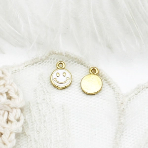 Detailed view of 18K gold plated smiling face charms with white enamel on lace background