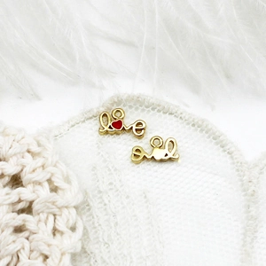 Detailed macro view of 18K gold plated Love charms with red heart on white lace fabric