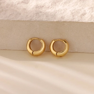 Detail of chunky gold hoop earrings with polished finish on a textured stone display