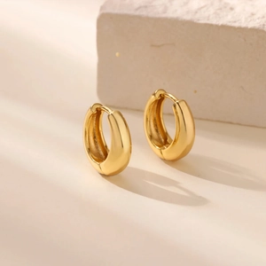 Macro detail of thick gold hoop earrings placed on a textured white decorative stone