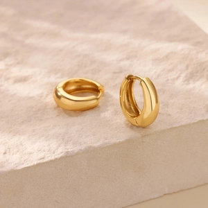 Minimalist wide gold hoop earrings with polished mirror finish on natural stone background
