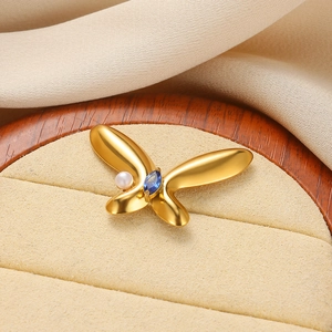 Dettaglio macro della spilla a farfalla dorata con perla bianca e gemma blu marquise