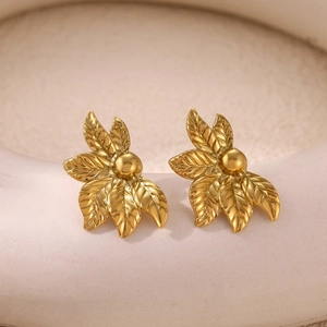 Close-up of golden floral earrings with brushed metal texture on a ceramic base