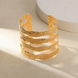 Détail d'un large bracelet manchette ouvert doré avec texture martelée et design ajouré