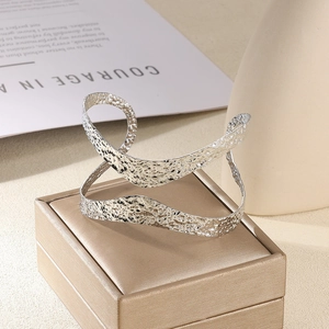 Détail de la texture martelée argentée sur un large bracelet jonc ouvert au design croisé